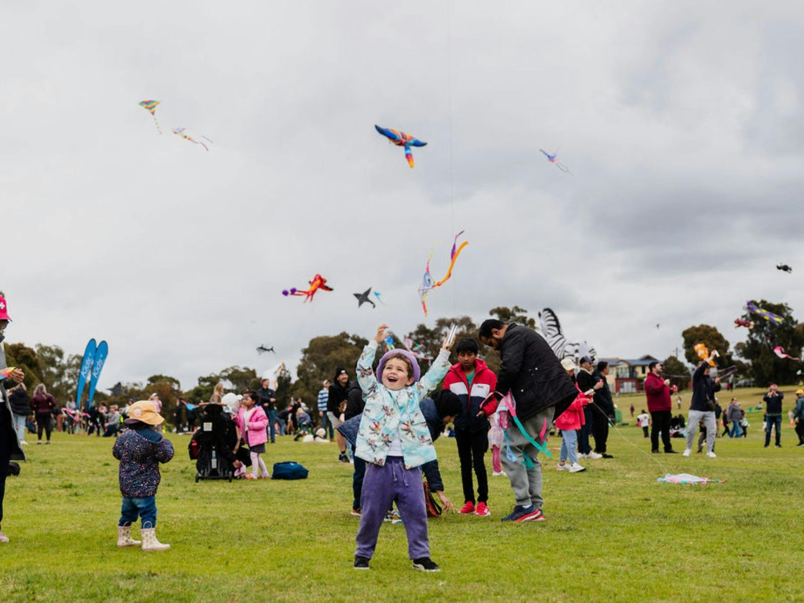 A small boy raising his arms excitedly as kites fill the sky above him