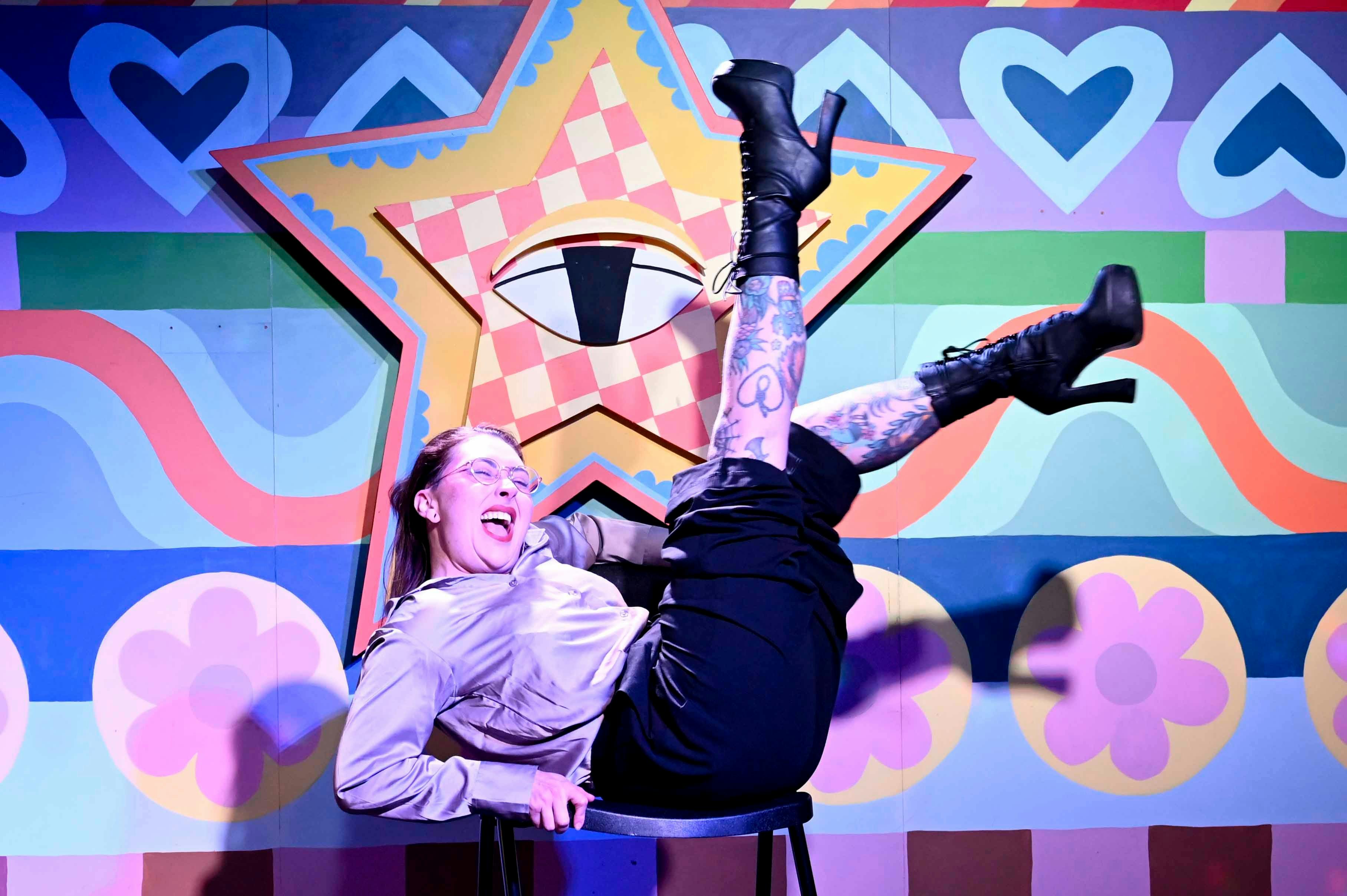 A woman in front of a star decal background, on the floor with legs in the air and laughing