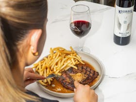 Guest enjoying steak and chips with a glass of red wine on table