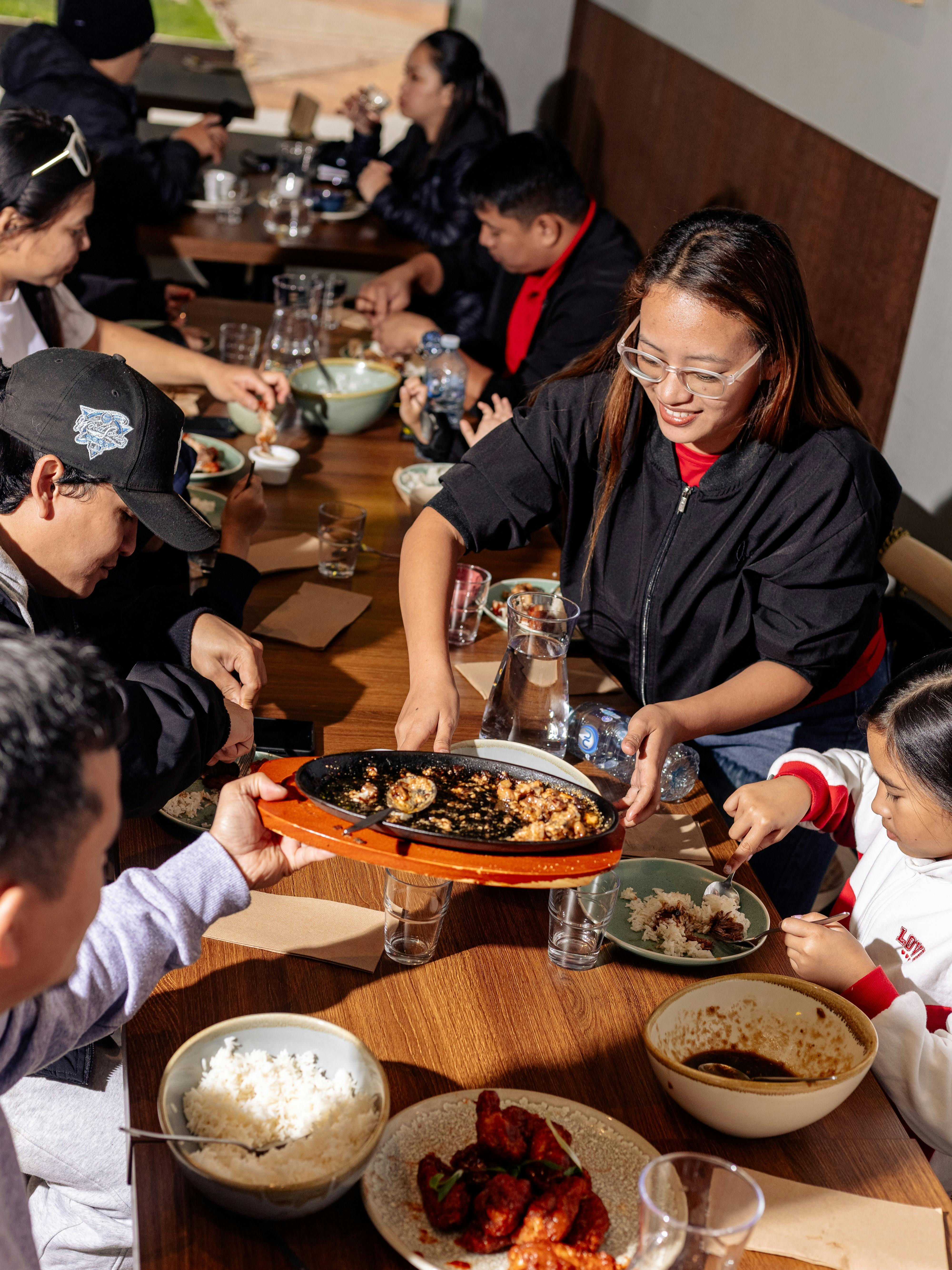 A group of people sitting around a dining table sharing Filipino dishes, with plates, bowls and drin