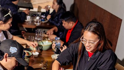 A group of people sitting around a dining table sharing Filipino dishes, with plates, bowls and drin