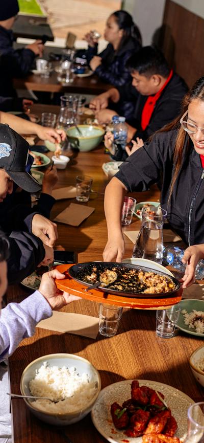 A group of people sitting around a dining table sharing Filipino dishes, with plates, bowls and drin