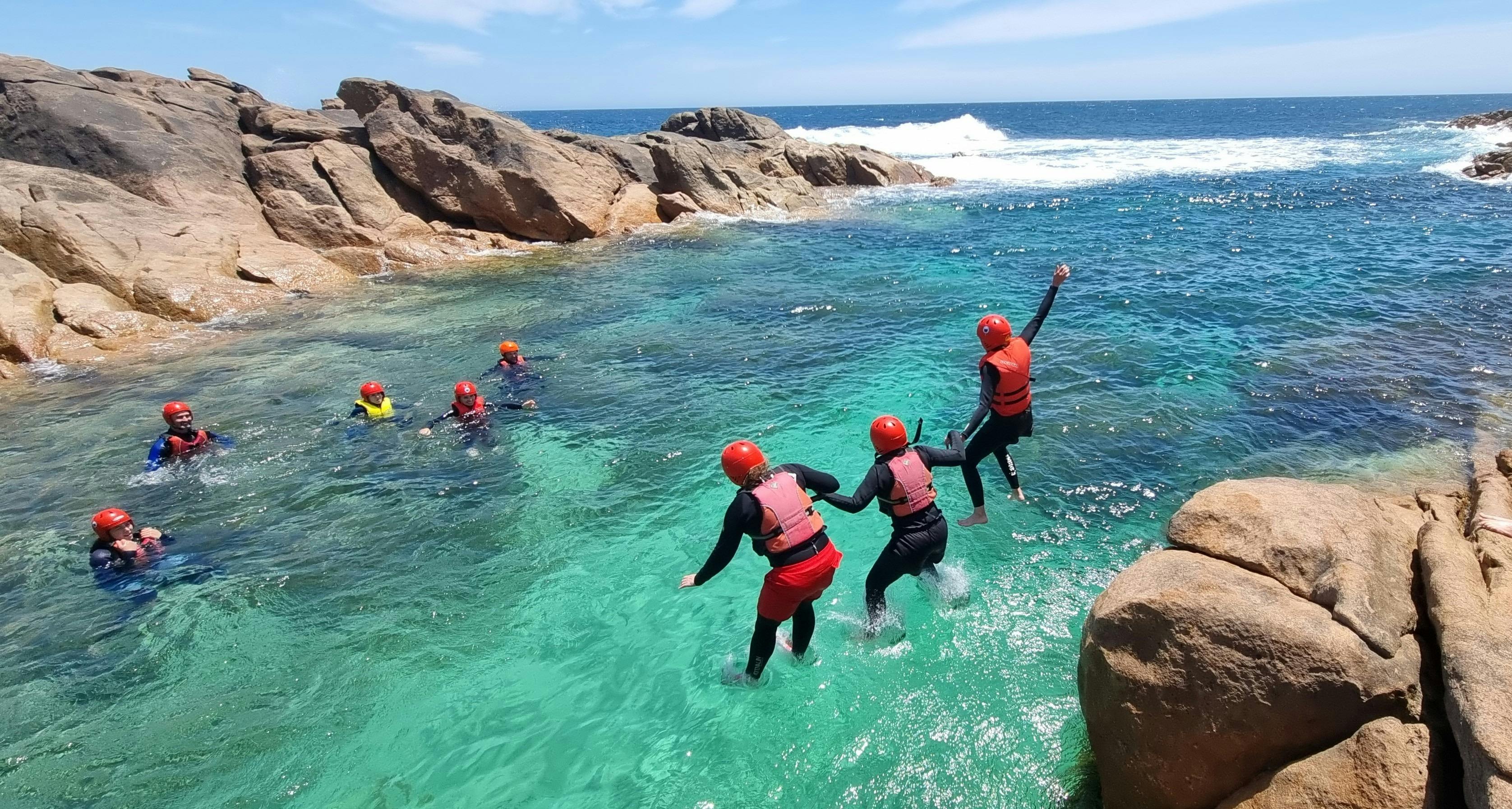 three hikers jump into water holding hands while remaining hikers in the water watch
