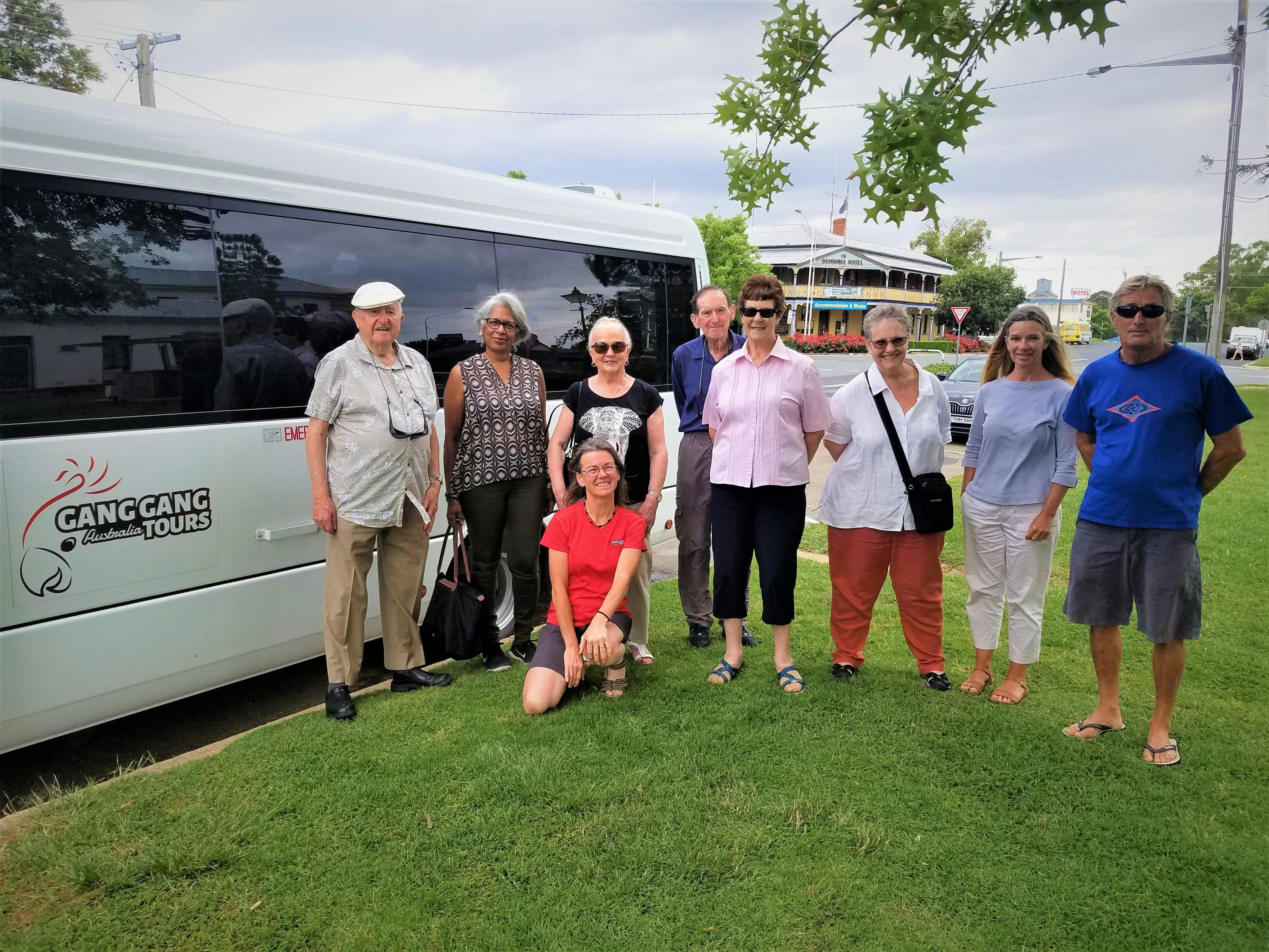 eight adults standing on grass in front of white tour bus