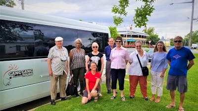 eight adults standing on grass in front of white tour bus