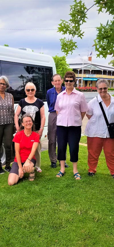 eight adults standing on grass in front of white tour bus