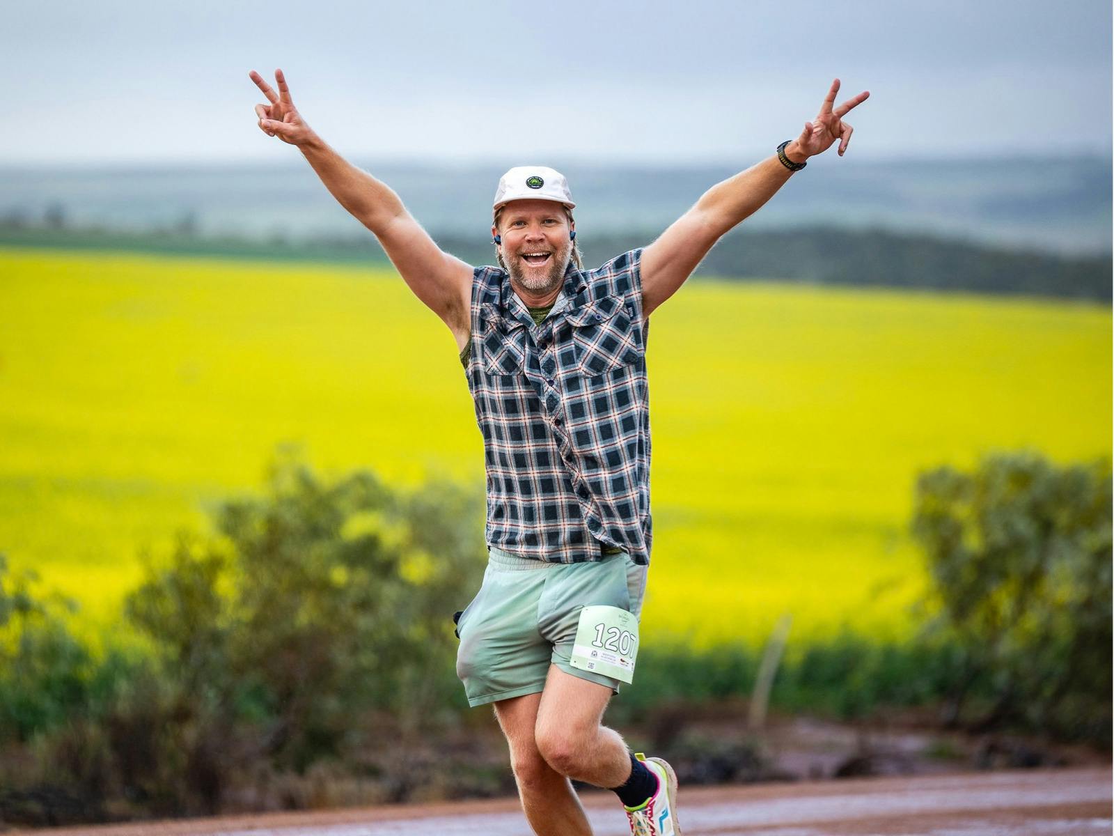 Smiling runner with arms raised in front of a yellow canola field.