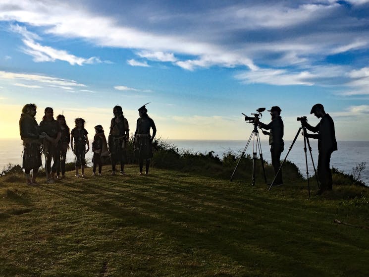 Two filmmakers and indigenous dancers on headland at sunrise