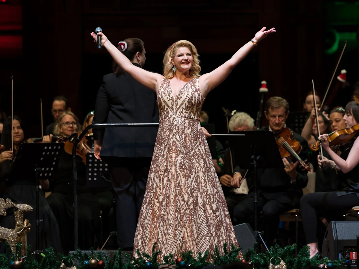 Glamous lady long gold beaded ballgown with arms in the air with Orchestra playing in background