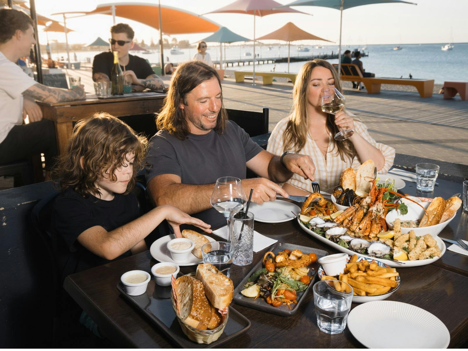 Family of three enjoying a delicious seafood meal beside the ocean