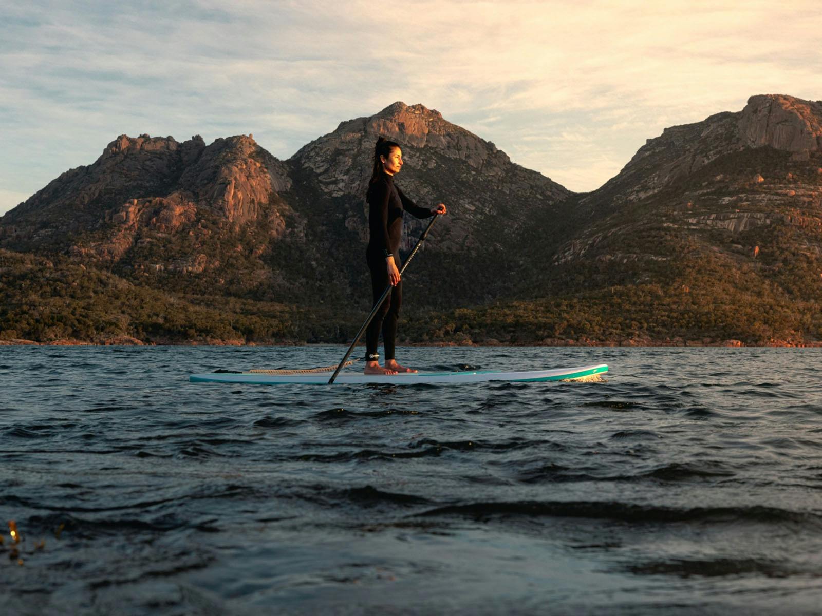 A women paddleboarding in Freycinet National Park with the backdrop of The Hazards mountain range
