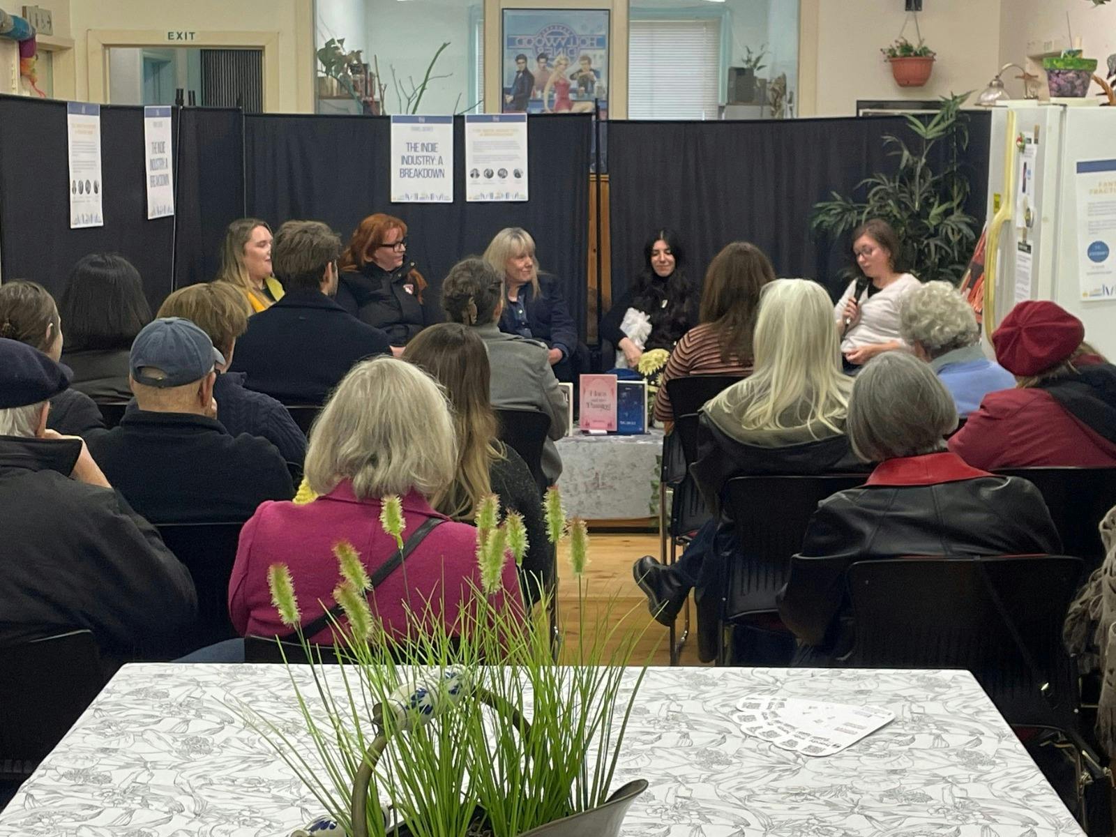 Background features five women talking about publishing industry. Back of audience in foreground,