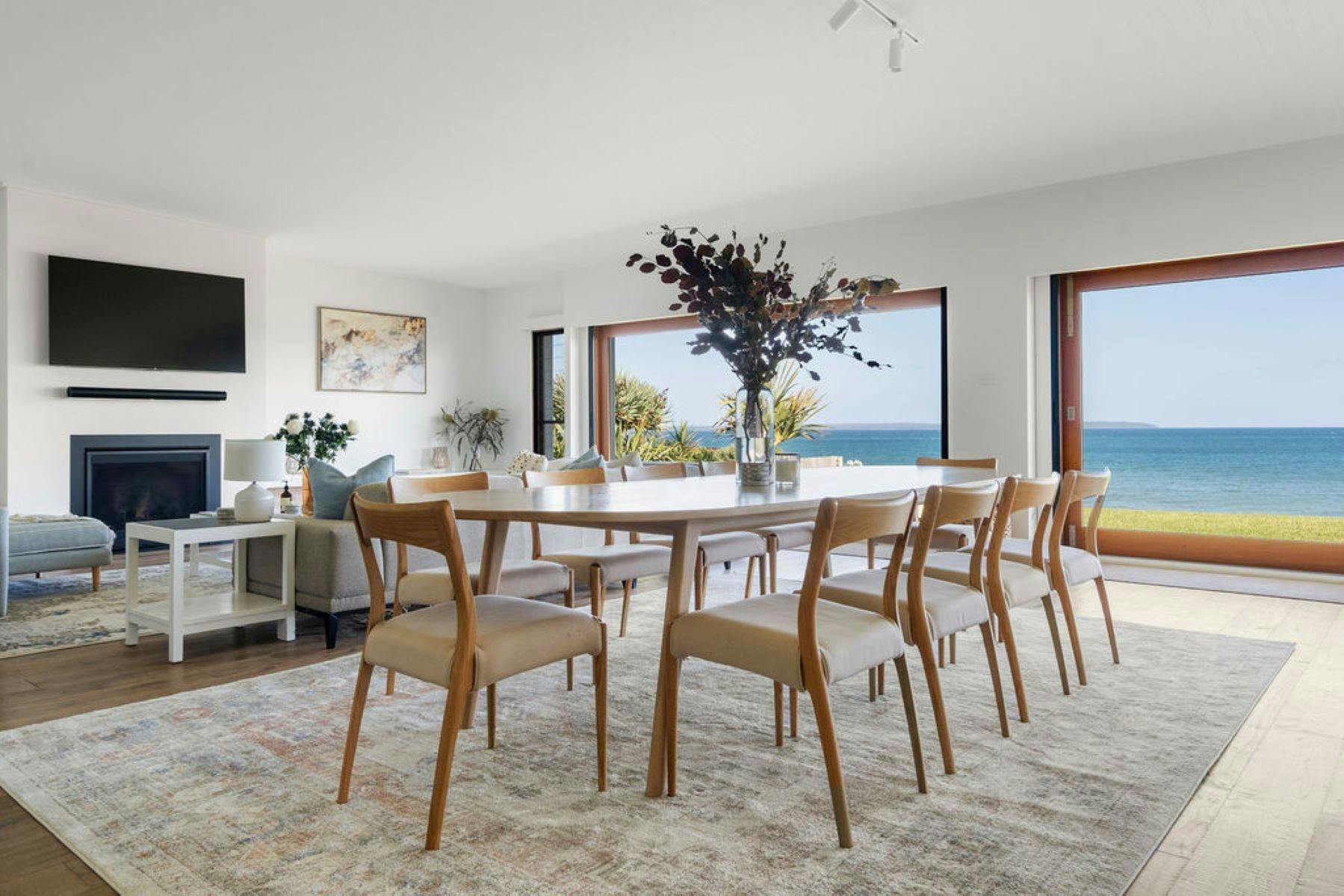 Image of inside dining area. Timber table with timber chairs surrounding table. View of ocean  seen.