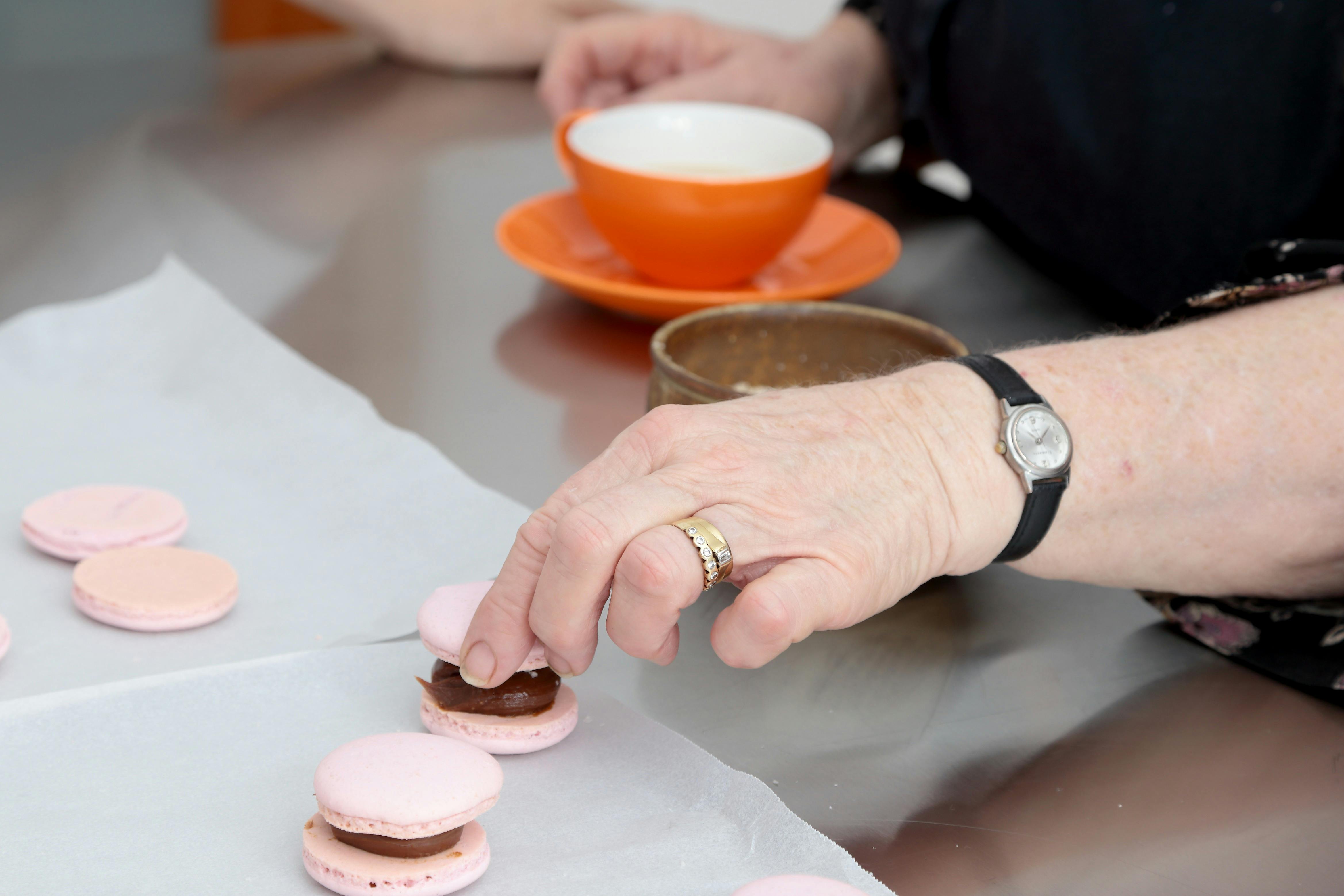 A hand putting the top shell on a pink macaron in the Jacican cooking school kitchen, Gippsland