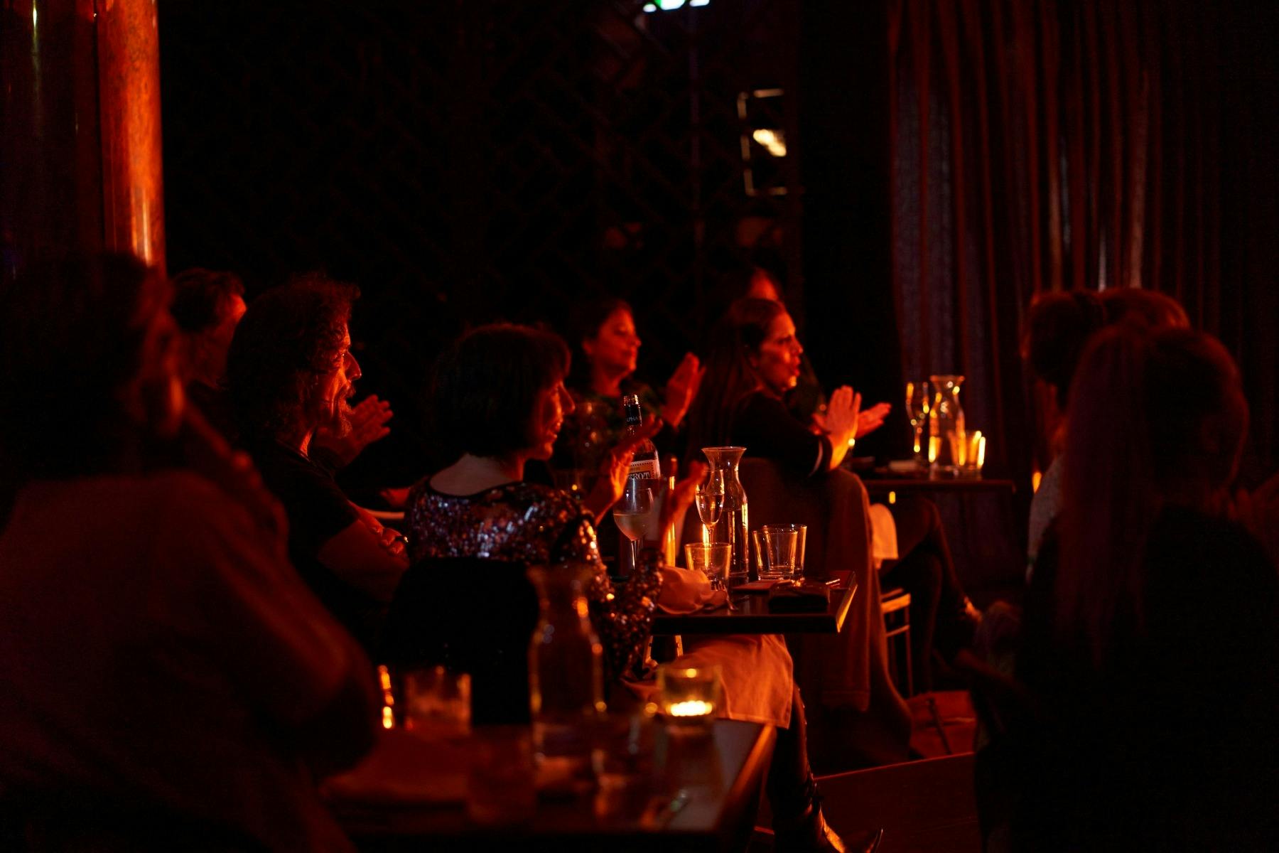A room full of people seated, clapping and facing the stage show intimate and cosy environment