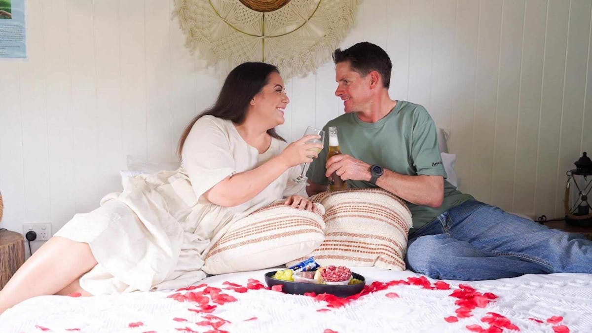 Couple Sitting on the glamping tent king bed with romantic package, rose petals and cheese platter