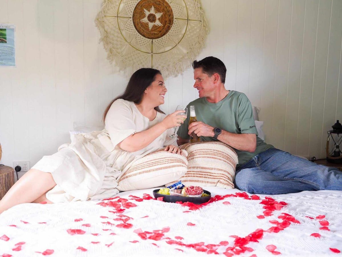 Couple Sitting on the glamping tent king bed with romantic package, rose petals and cheese platter