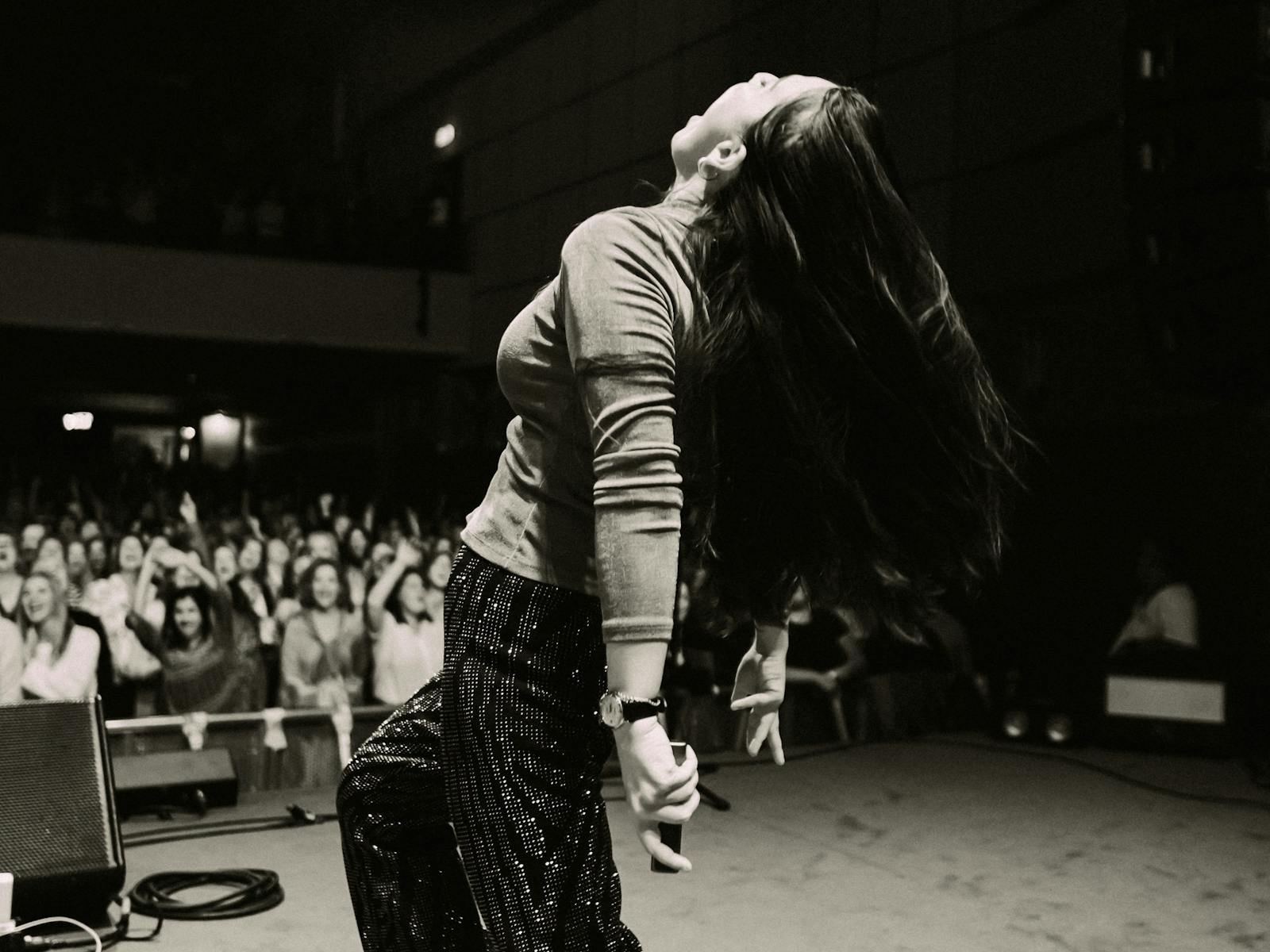 a woman holding a microphone with her head thrown back in front of a crowd