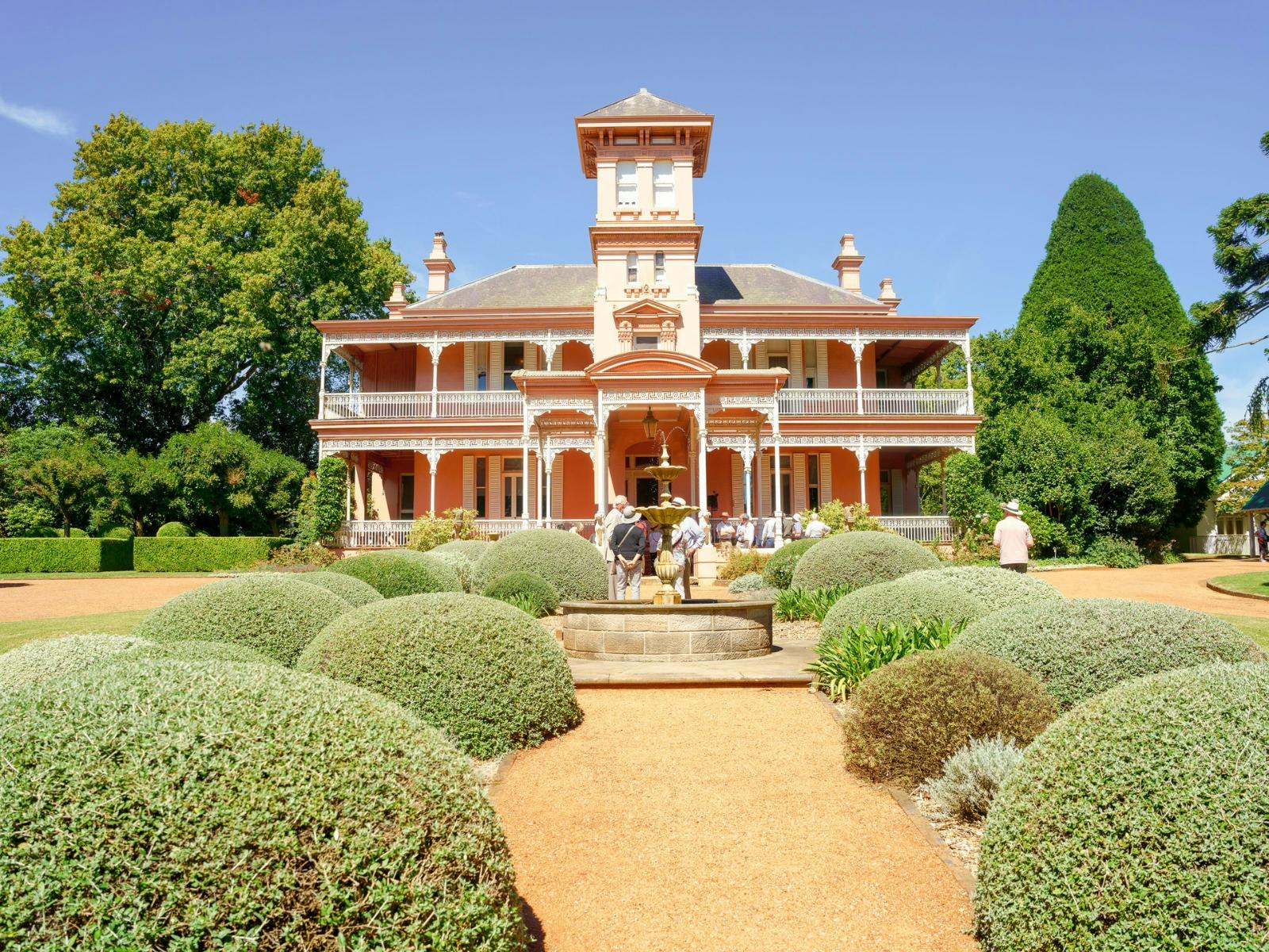 Double storey pinkbuilding stands proudly against a blue sky, surrounded by tall trees.