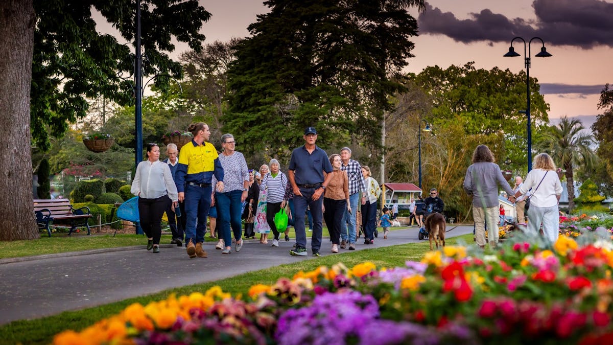 A gardener leads a group of people through a park at twilight.