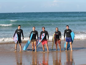 A group of surfers stand together at the waters edge after a surf lesson