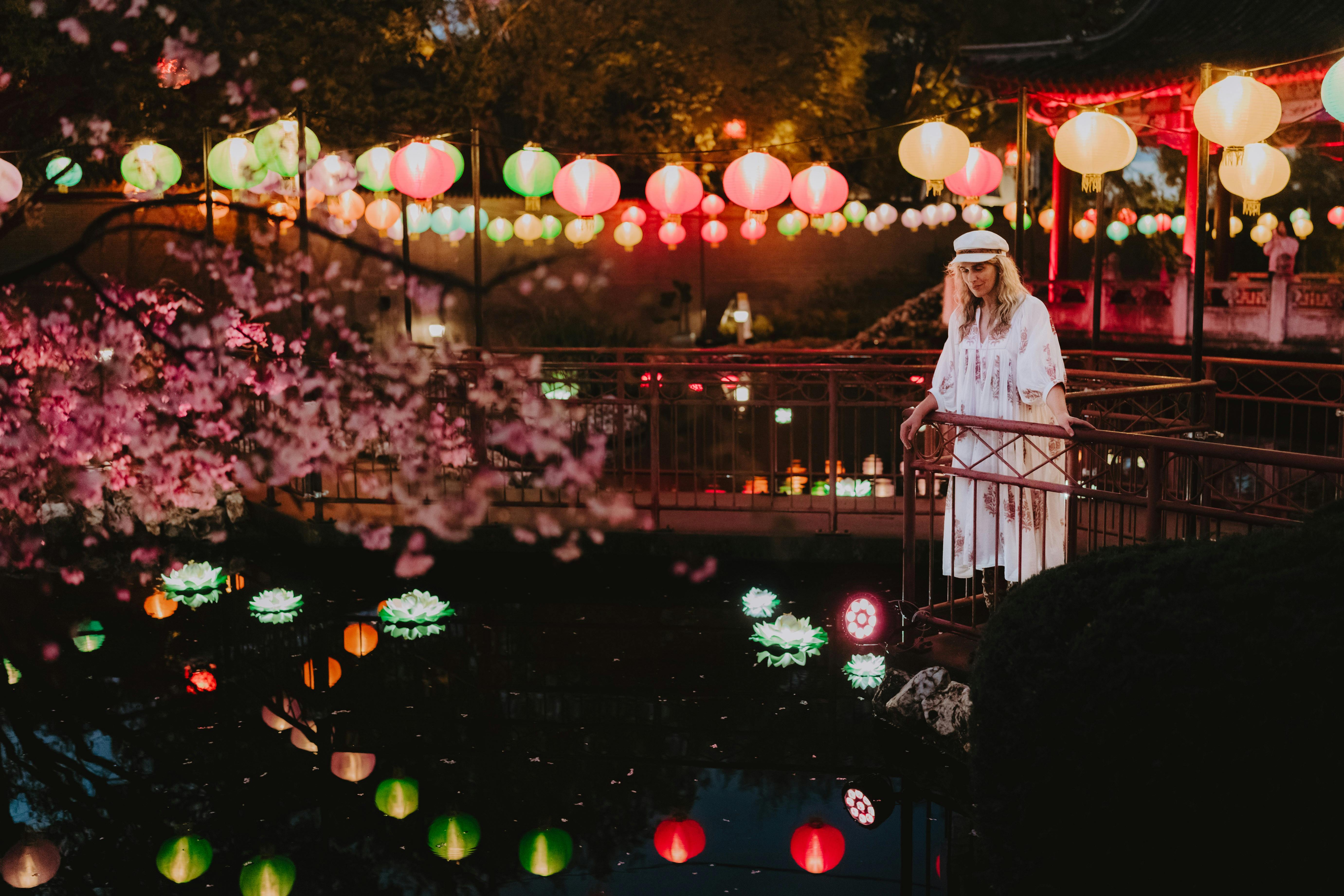 A lady walking down a path in the Yi Yuan Gardens at light. She's looking at rainbow lanterns