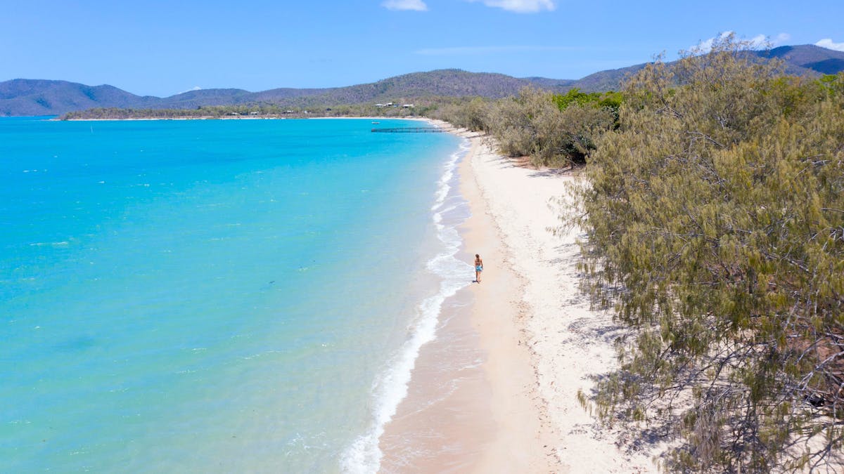 A woman walking along the calm turquoise water of Dingo Beach