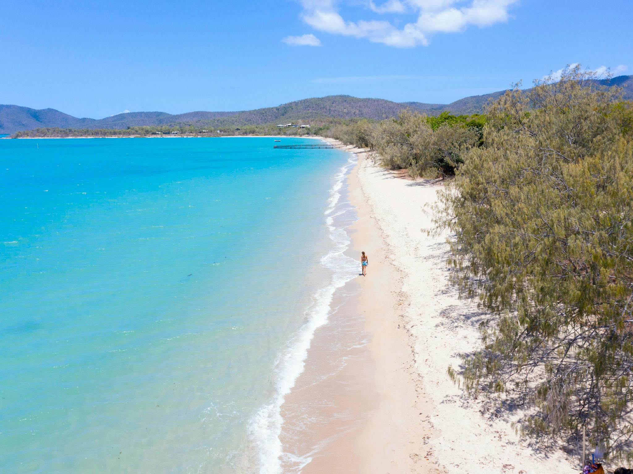 A woman walking along the calm turquoise water of Dingo Beach A woman walking along the calm turquoise water of Dingo Beach