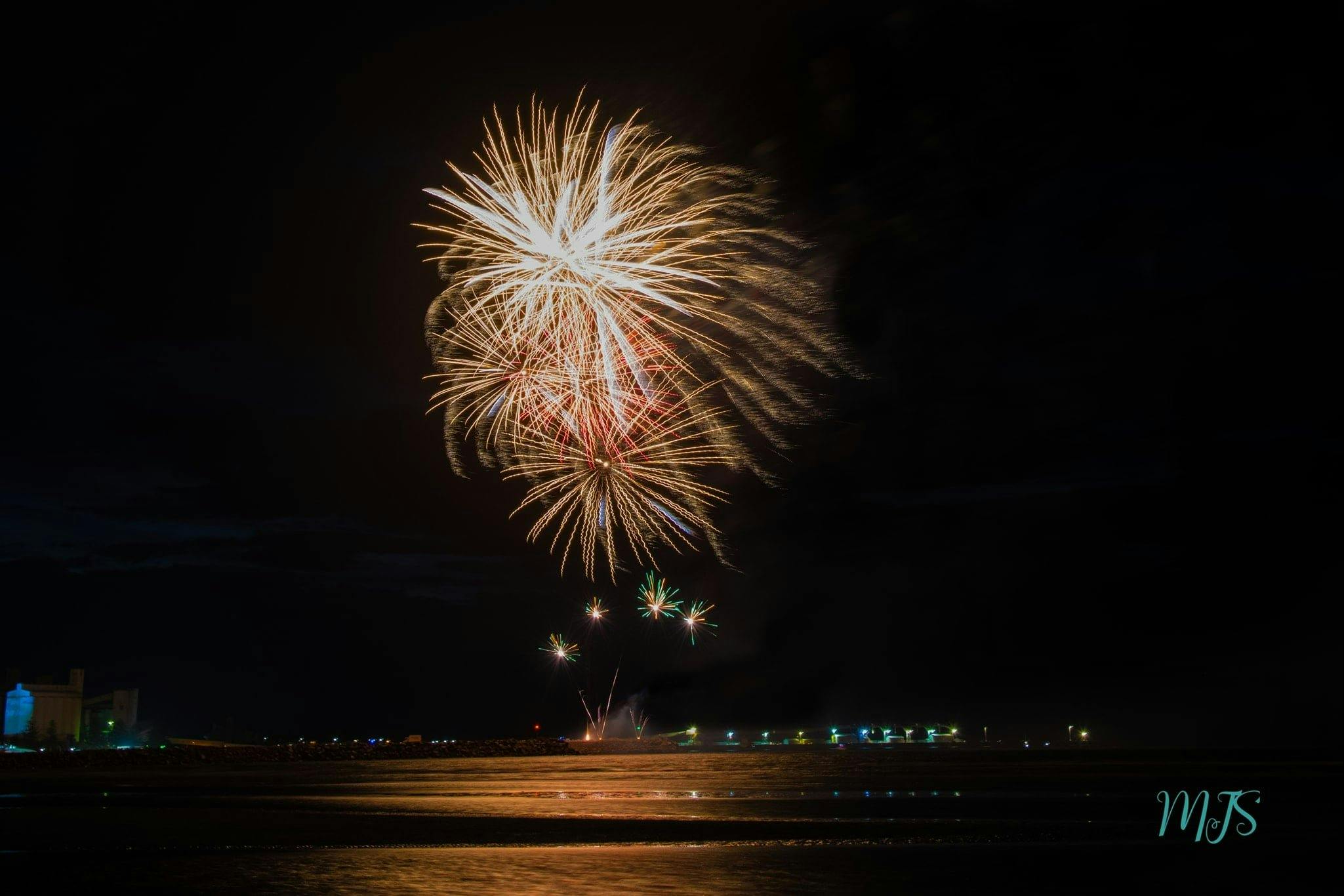 4 large golden fireworks exploding over the night sky and sea.