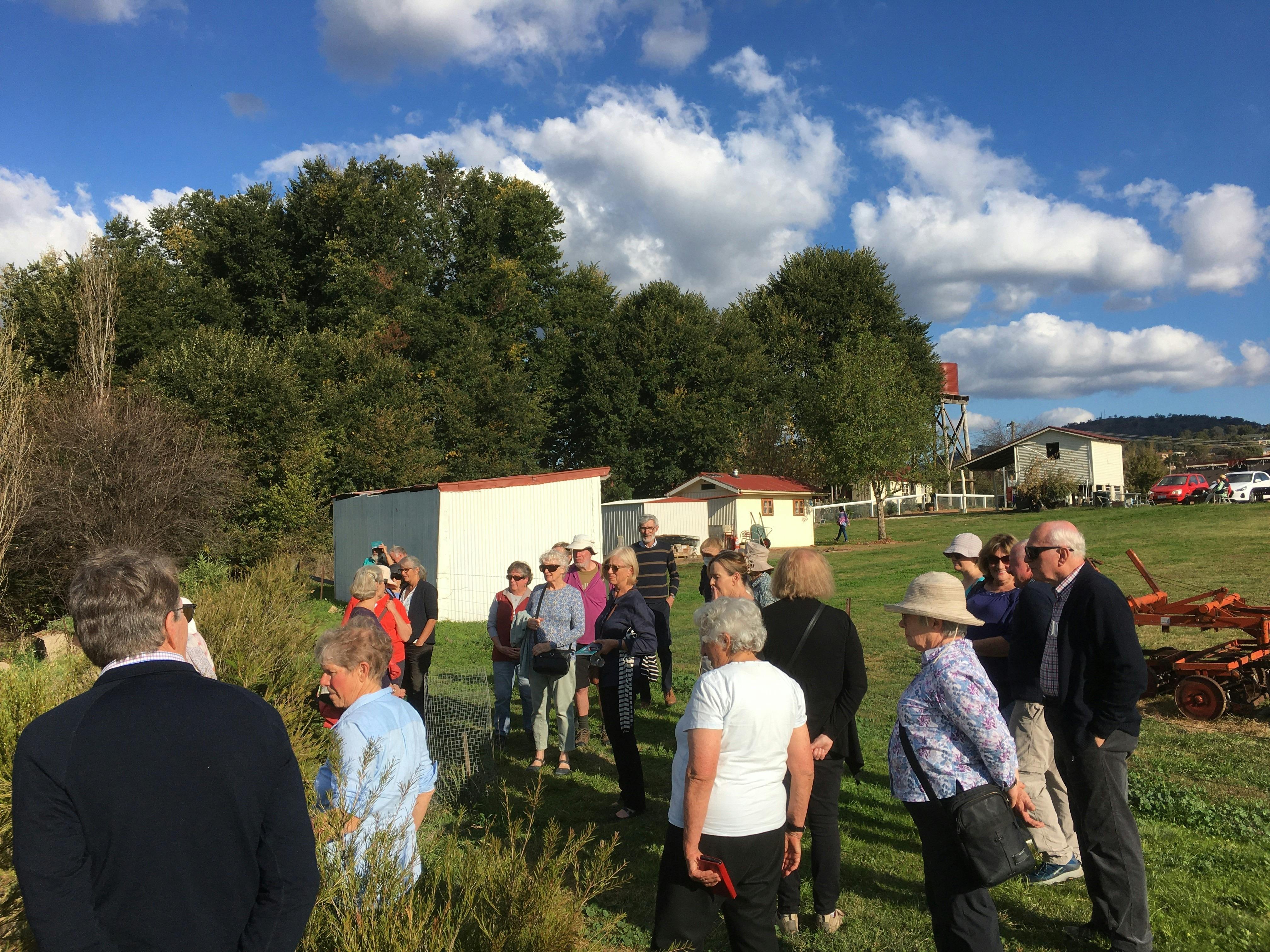 group of 20 people standing outside in rural setting with farm out buildings in background