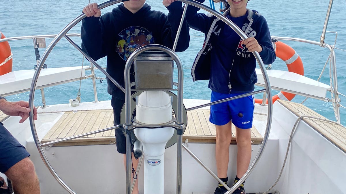 Two children with captains hats on steering the yacht on Sun Sailing's midday shared cruise