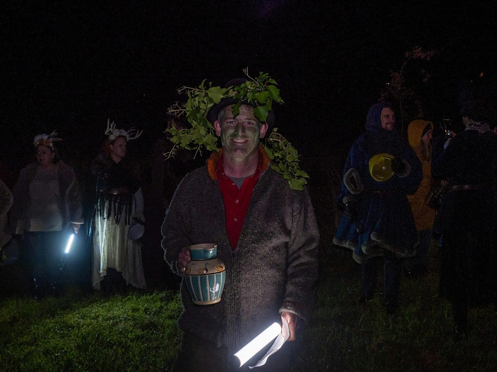 Man wearing green makeup and trees carrying  a porcelain jug