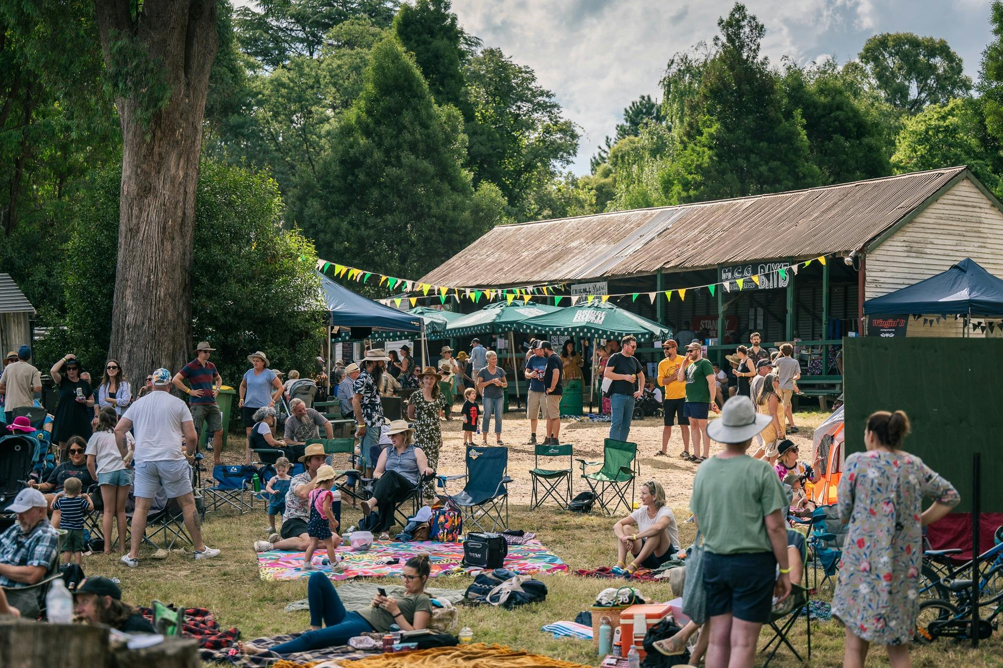 A historic pavilion with a crowd of people in front with a beautiful backdrop of tall trees