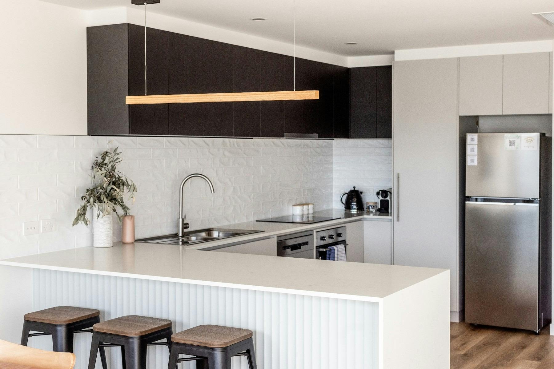 "Contemporary full-size kitchen featuring stone benchtops, quality appliances, breakfast bar seating