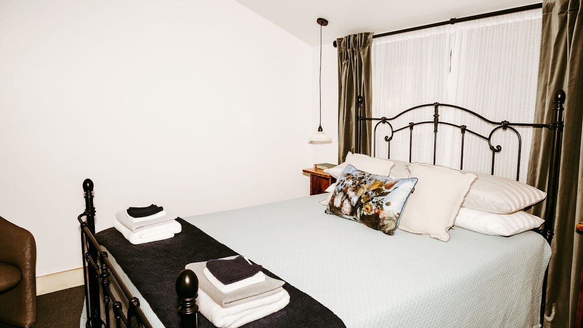 Black wrought iron bed with pale blue and dark blue linen and a floral feature cushion and towels.