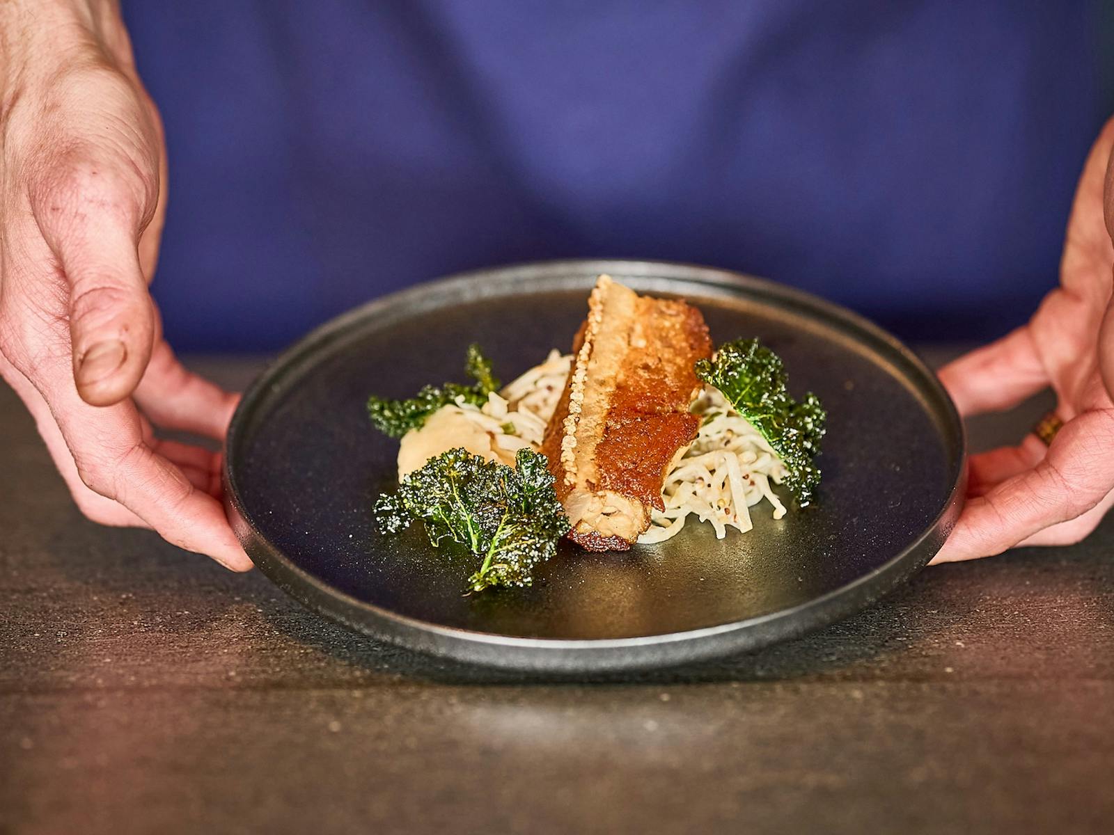 Chef holding plate, presenting pork belly, celeriac remoulade, apple & cavolo nero
