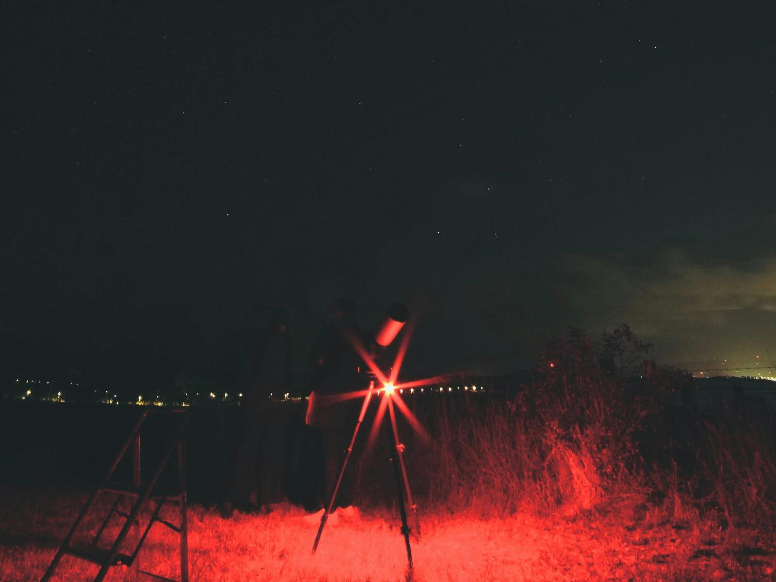Telescope on a dark night with red tour lighting and stars visible overhead.