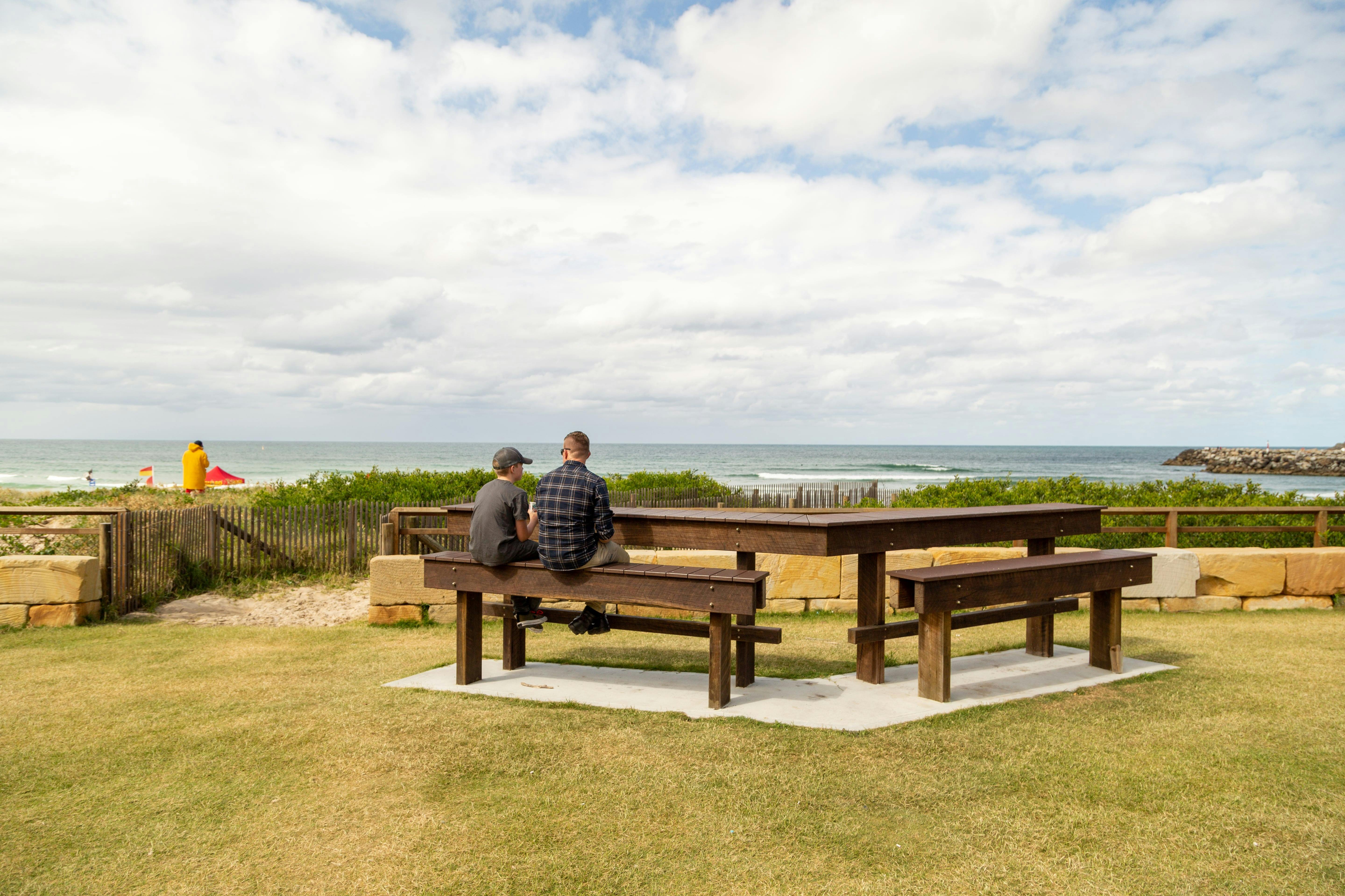 A man and son sitting on a picnic table admiring the beach