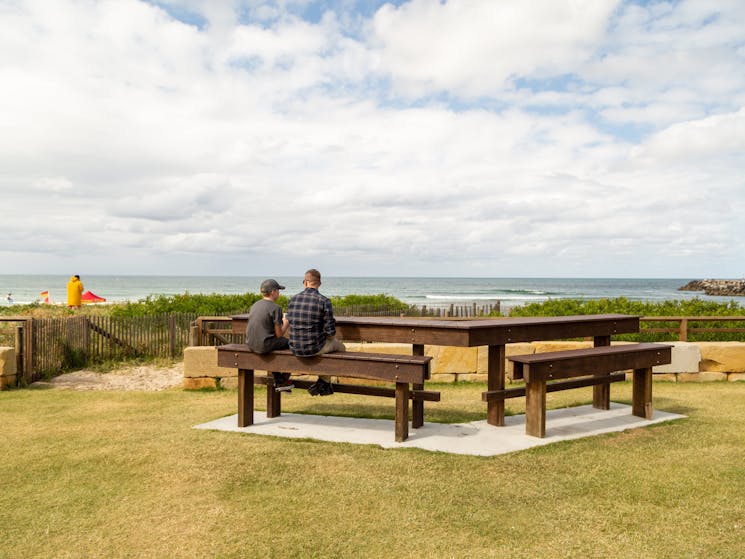 A man and son sitting on a picnic table admiring the beach