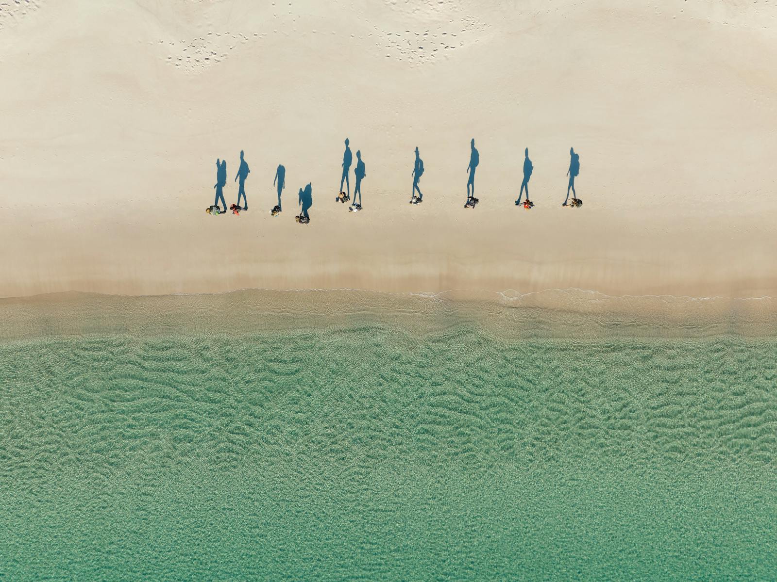A group of hikers all walking single file down a beach from an arial view