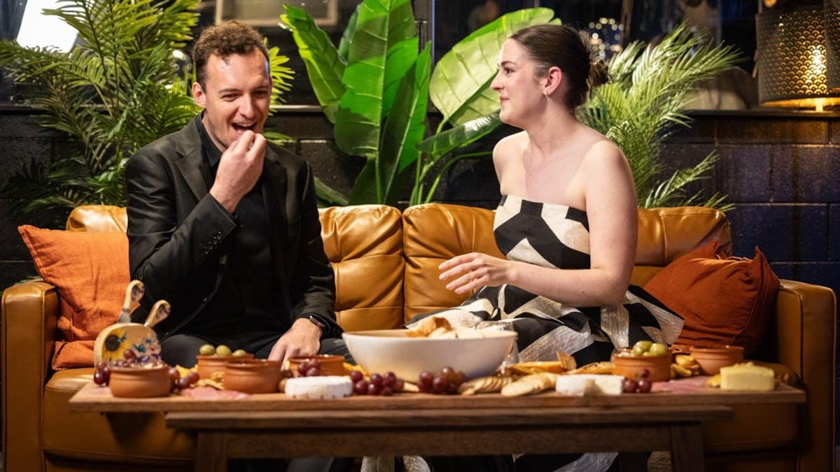 People sitting and talking on a brown leather couch with a cheese board Infront of them