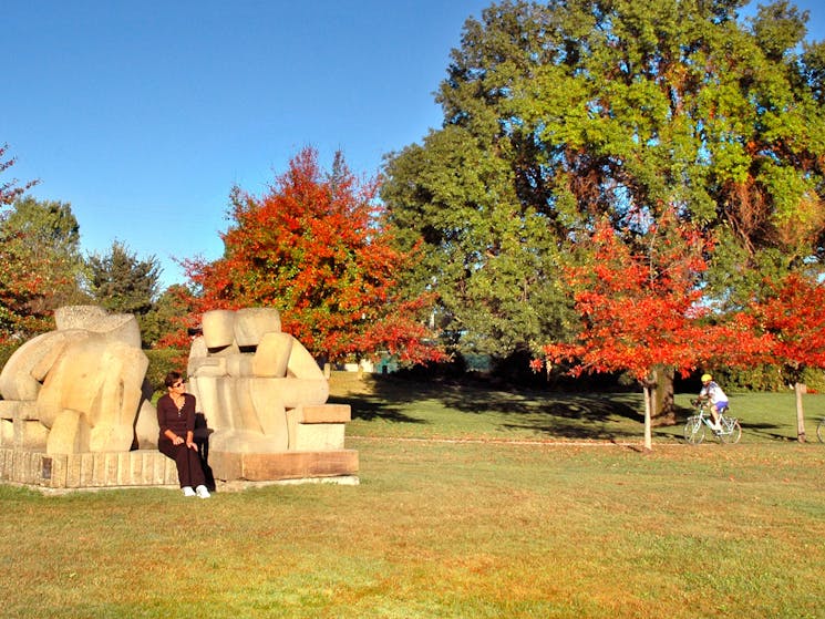 2 sandstone sculptures of people sitting down talking in the park.