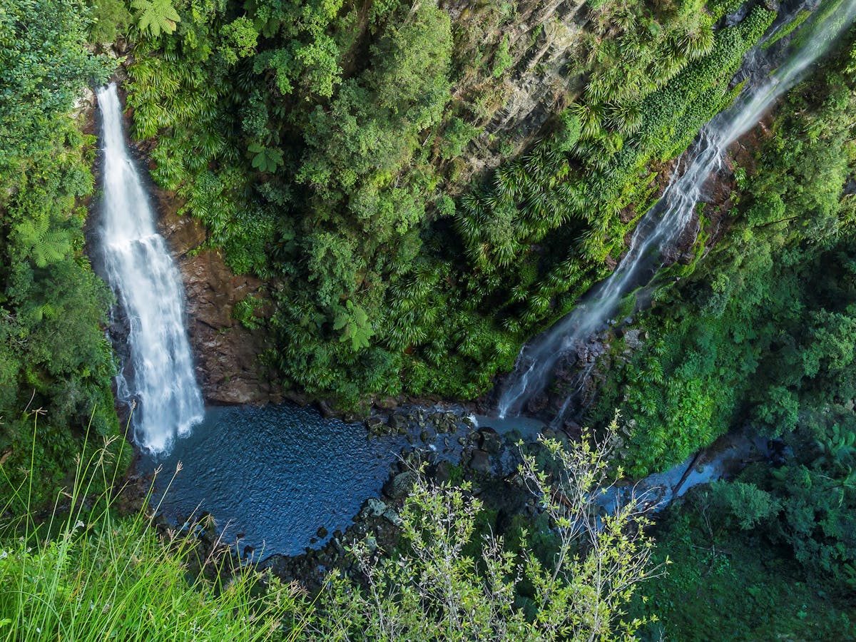 View down sheer rock wall with two waterfalls and pool at bottom.