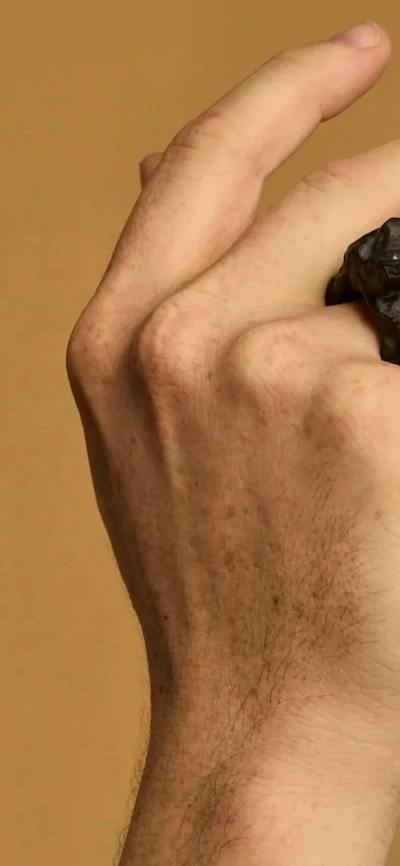 A hand wears a large ring carved out of a dark material against a tan background