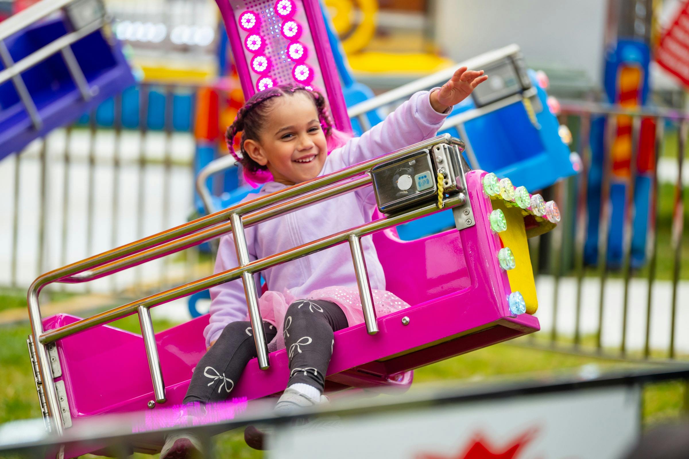 young girl smiling in a purple dress on a colourful spinning ride