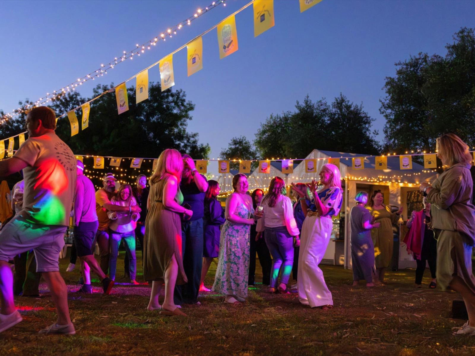 Group of people dancing under fairy lights and bunting at dal zotto prosecco festival