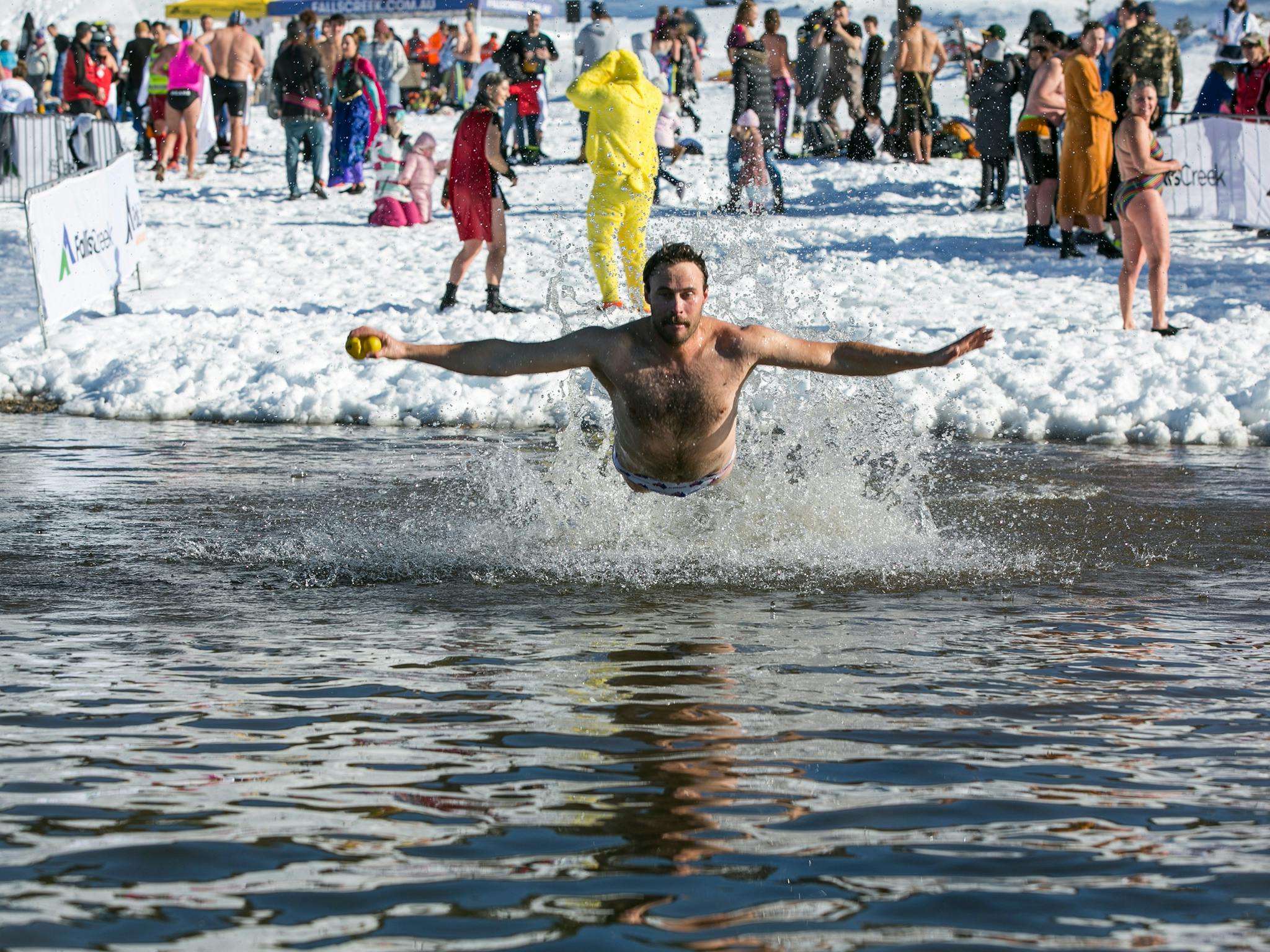 A man in swim trunks diving into a lake with snow on the ground behind