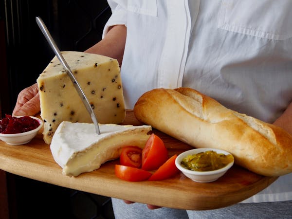 A close up image of a cheese platter with olives, cut up tomatoes, bread loaf, chutneys