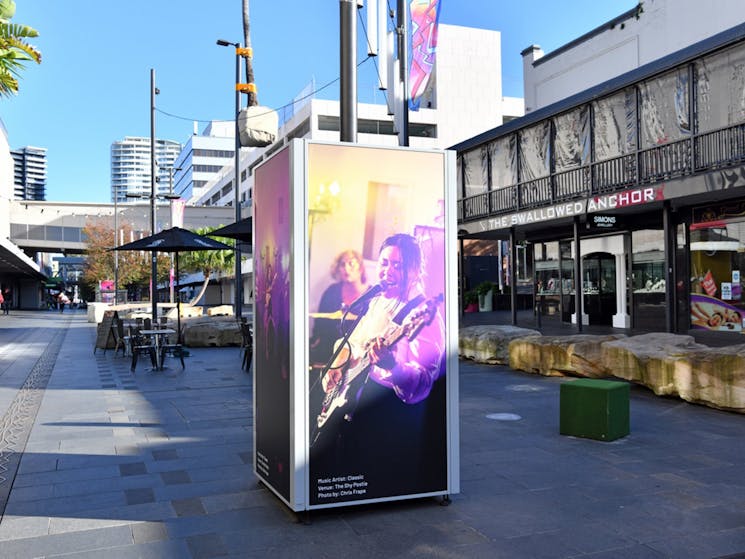A large scale photograph of a singer is on exhibit in an outdoor mall.