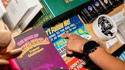 A close-up of a shopper’s hand browsing a selection of Canberra-themed books, stickers